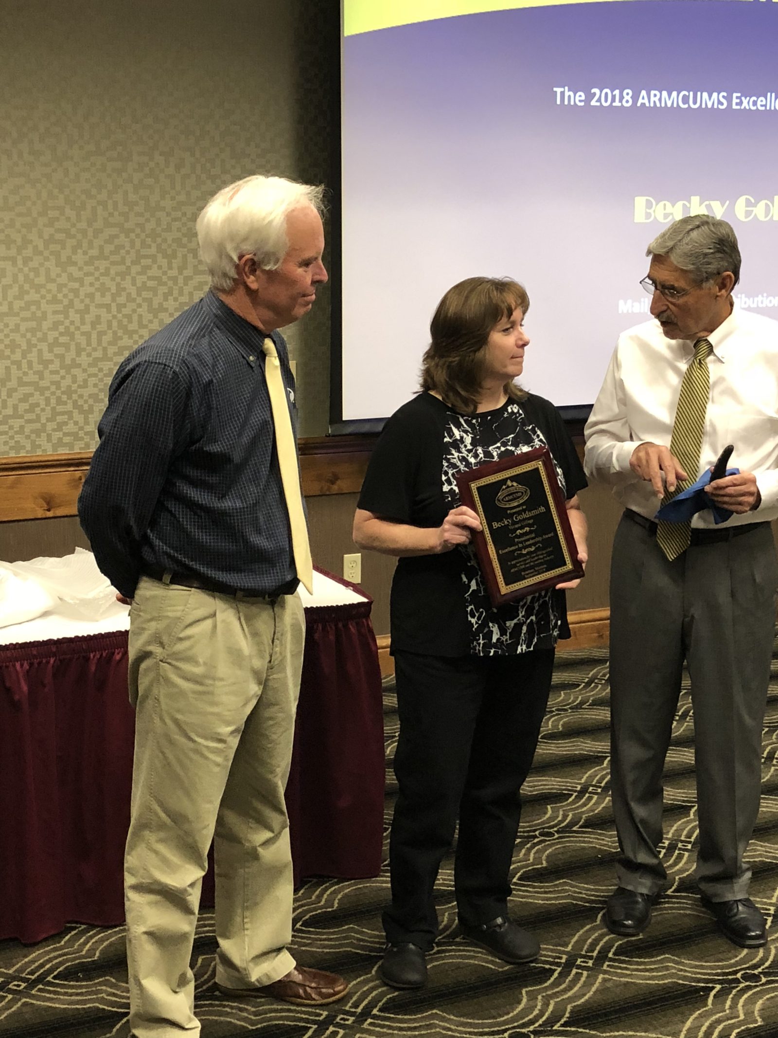 Three people stand together during an award ceremony, with one holding a plaque.