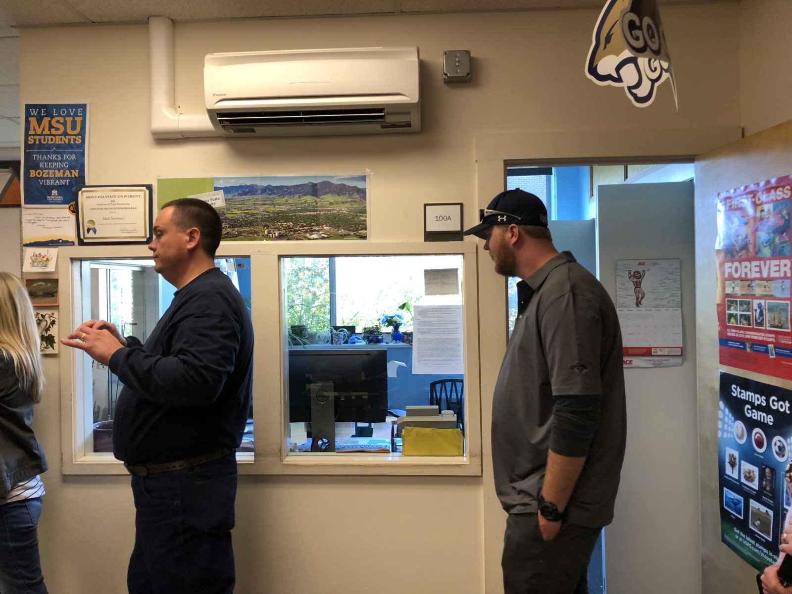 Two men standing in a small room near a window and vending machines.
