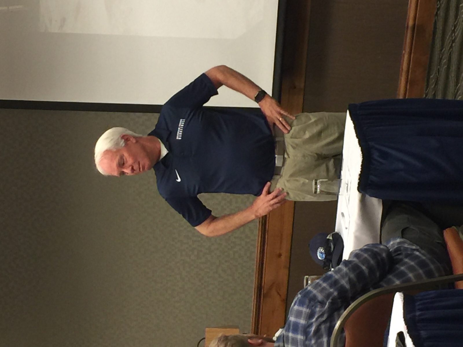 A man stands and speaks in front of a small audience in a classroom.