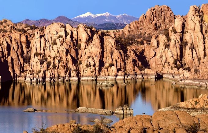 Rocky cliffs reflected in calm water under a clear blue sky.