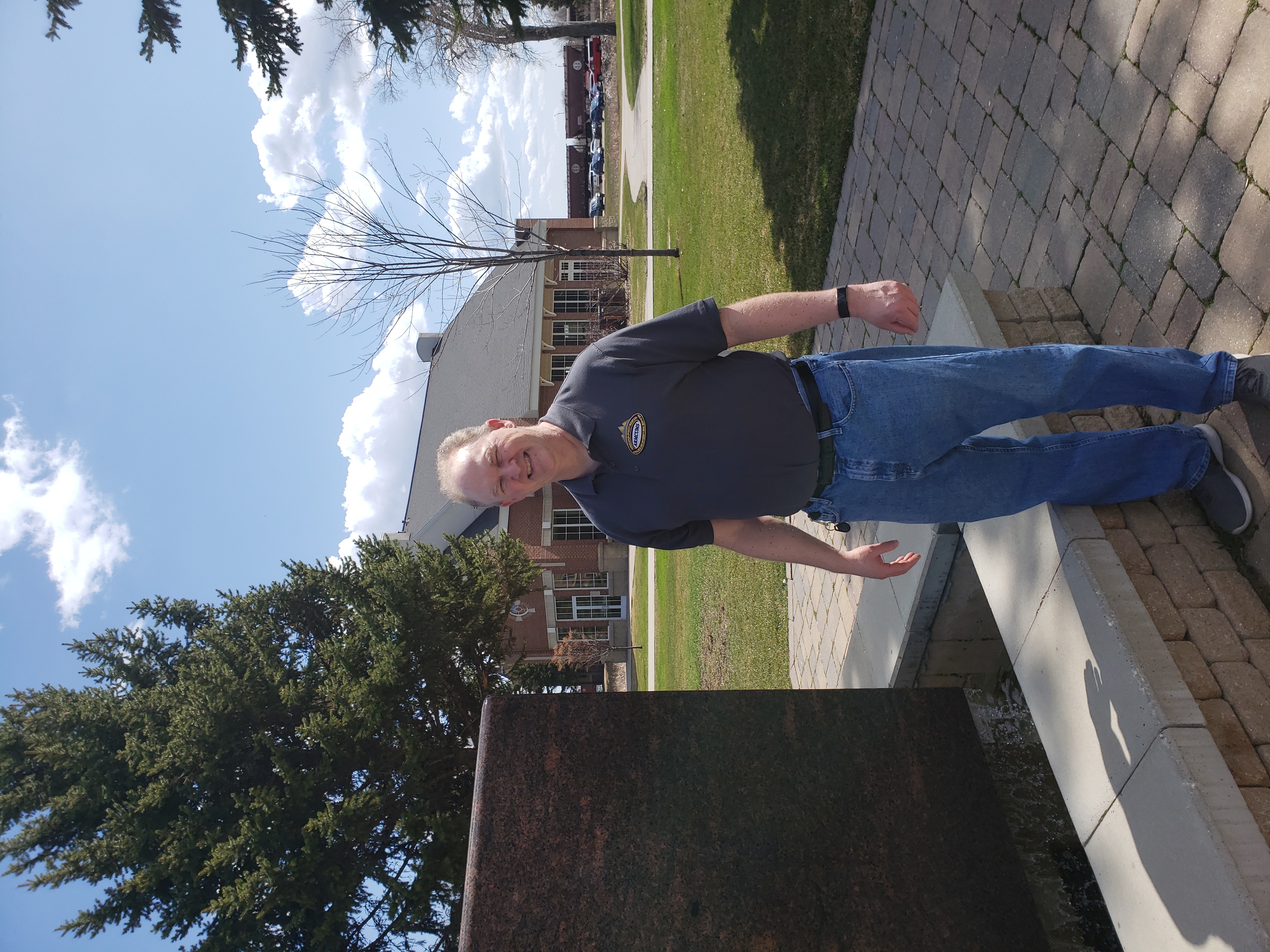 A man standing outdoors near a stone water feature on a sunny day.