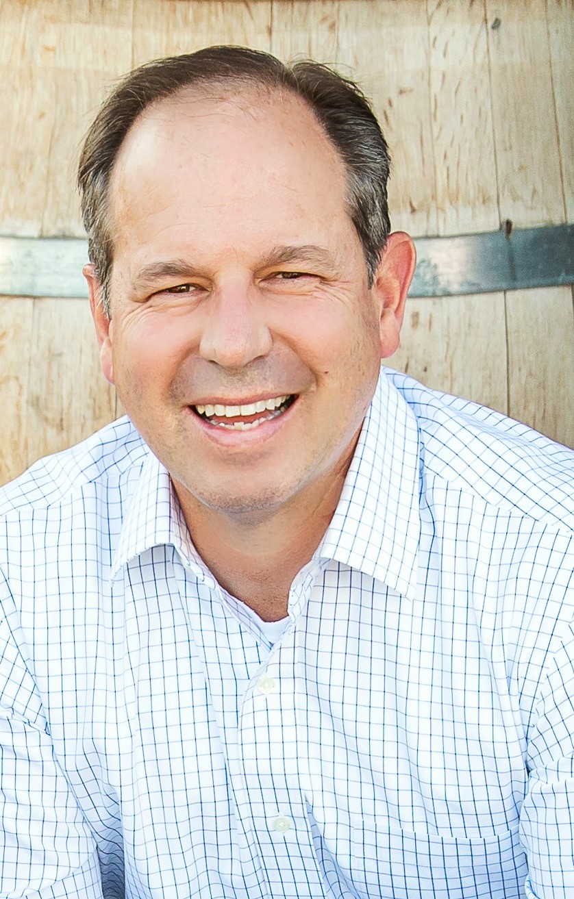 Smiling middle-aged man in a checked shirt outdoors.