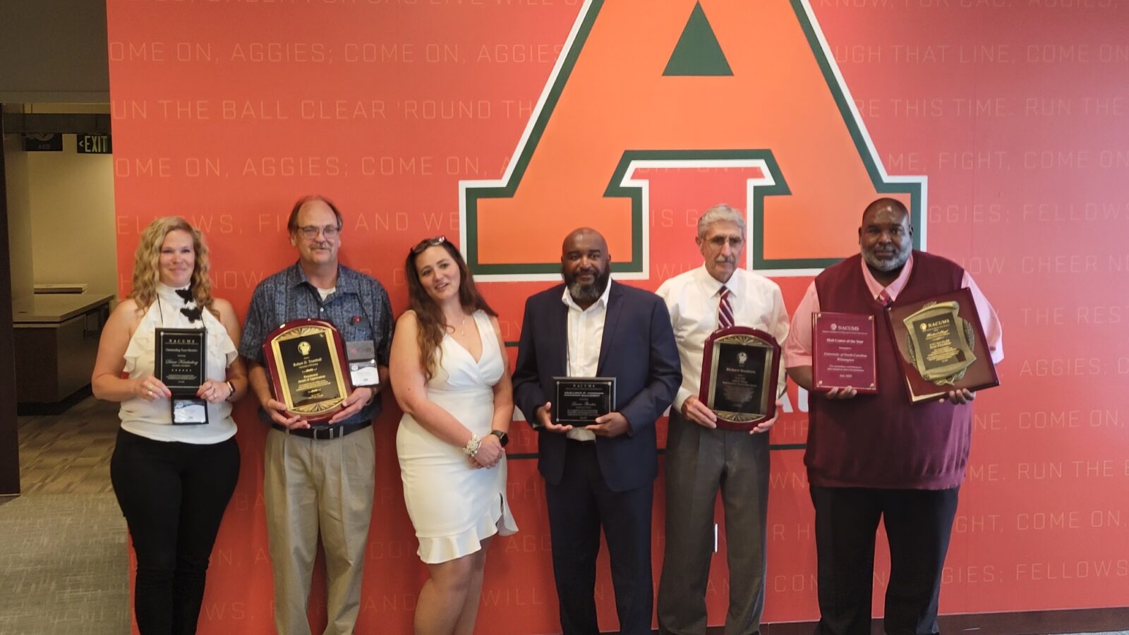Five people holding awards, standing in front of a large letter A.