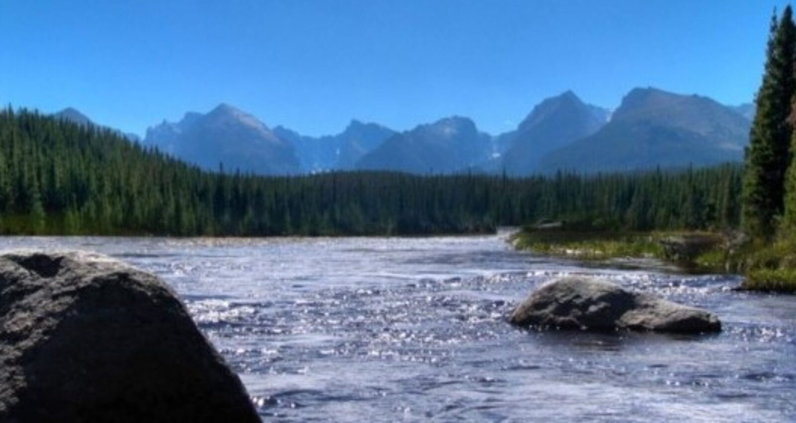 A wide river flows with mountains in the background under a clear sky.