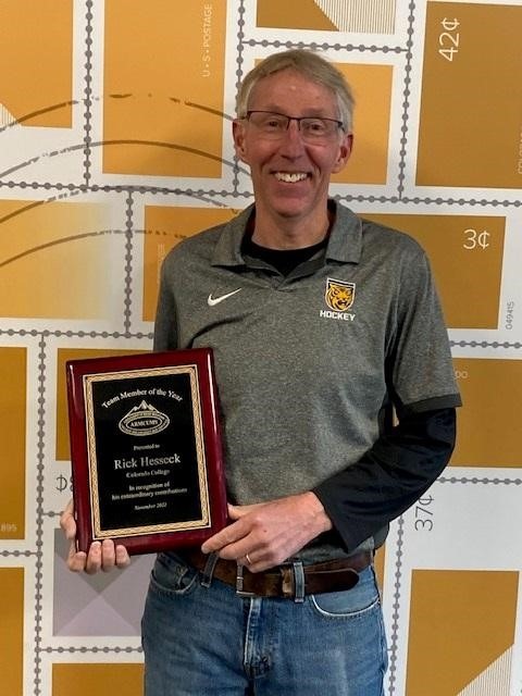 Man holding plaque, smiling, against stamp backdrop.
