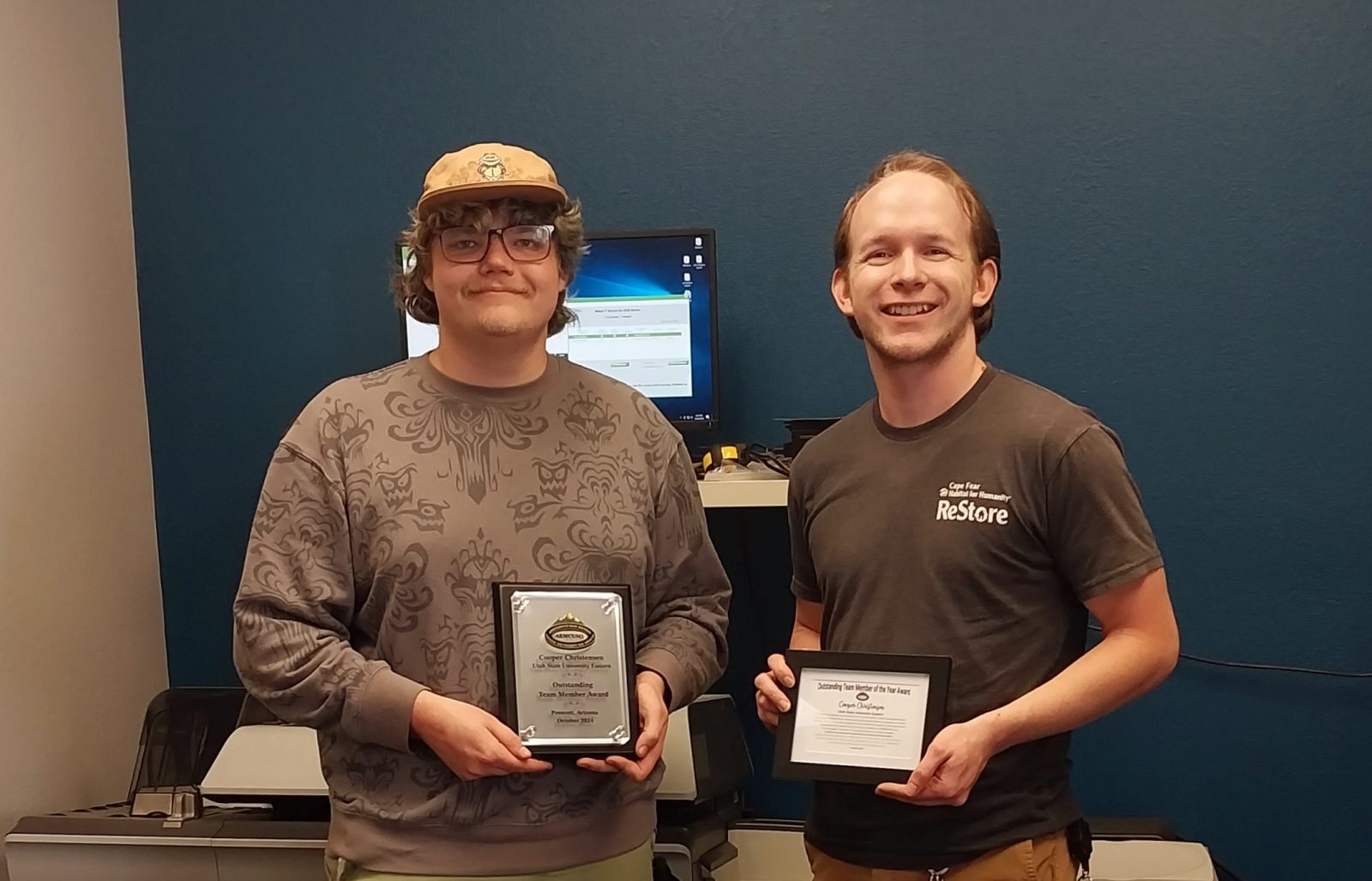 Two people holding awards, smiling indoors.