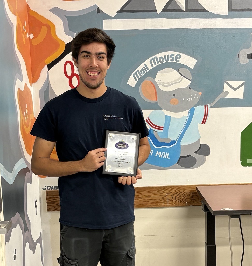 Man holding an award, smiling near mural.